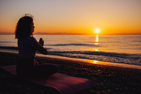 Carefree woman sitting in yoga mountain pose by the sea sunrise time. Finding inner peace spiritual healing lifestyle. Stretching in the morning for increasing energy.の写真素材