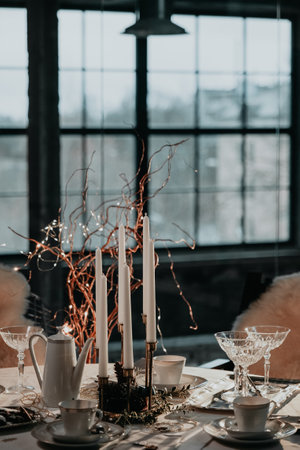 Christmas table setting, cups, teapot, candles, glasses served on white tablecloth. Preparing for cozy Christmas lunch, dinner or teatime.の写真素材