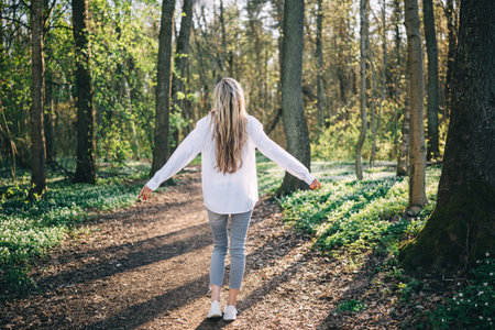 Rear view of young woman arms raised enjoying fresh air in spring forest. Enjoying nature. Freedom conceptの写真素材