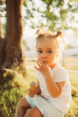 Adorable 2 years old girl eating ice cream outdoors at park, summer timeの写真素材