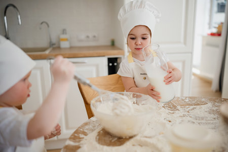 Adorable boy ad girl in chefs hats and aprons playing with the flour in the kitchen. Kids knead the...
