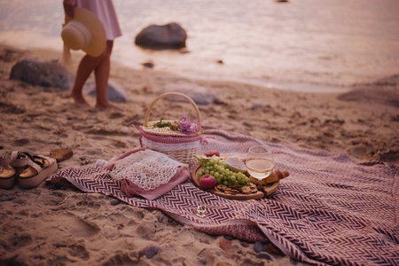 Beautiful summer picnic served for one person at sunset on beach with white wine, croissants, cookies, and fresh fruits. Woman legs on backgroundの写真素材