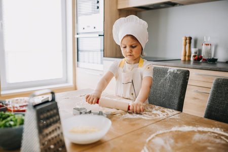 Adorable girl in chef hat and apron rolling out pastry dough at the kitchen. Young helper, preparing delicious pastry food.の写真素材