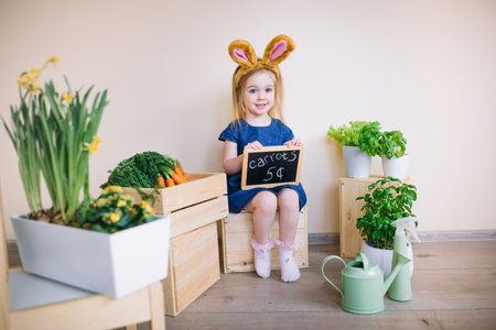 Cute little child girl wearing bunny ears on Easter day. Funny 3 years old girl holding price board,...