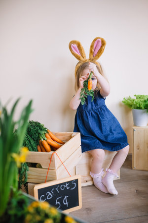 Cute little child girl wearing bunny ears on Easter day. Funny 3 years old girl hiding behind carrot
