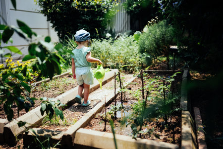 Adorable girl in summer clothes watering tomato plants growing in garden bed with watering can....