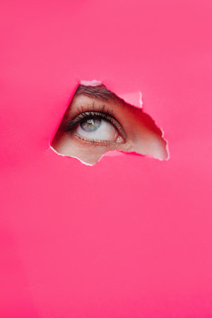 Eye of the beautiful woman looking up in the hole in pink paper. Glamour woman beautyの写真素材