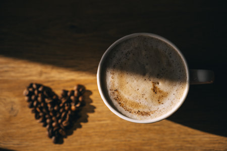Cappuccino cup on the table. Beautiful sun shining, coffee beans lying on the table in heart shapeの写真素材