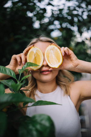 Outdoor portrait of beautiful young woman with smooth skin hiding her eyes behind halved lemon fruits. Skin careの写真素材