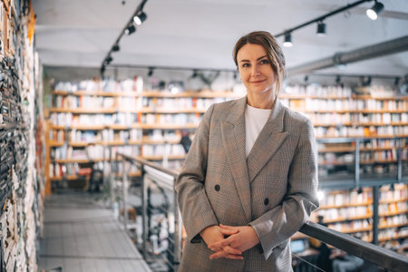 A woman in a plaid blazer stands in a modern bookstore, surrounded by bookshelves. She looks directly at the camera with a confident smile.の写真素材