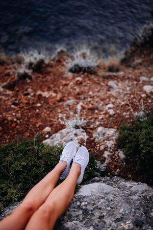 A person sits on rocky terrain, with their feet on the edge, overlooking calm waters and surrounding...