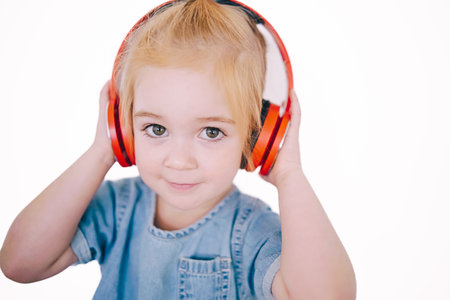 A joyful toddler adjusts her vibrant headphones, lost in the music, showcasing a playful moment of musical enjoyment at home.の写真素材