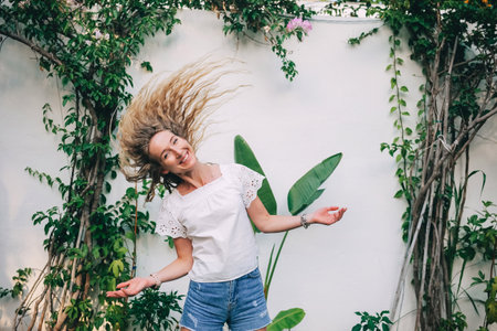 A young woman stands in a garden, her hair waving gracefully as she poses joyfully in a sunny atmosphere.の写真素材
