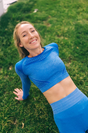 Athletic woman in blue sports clothing performs reverse plank exercise in the park. Morning...