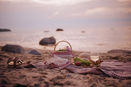 Beautiful summer picnic served for one person at sunset on beach with white wine, croissants,...