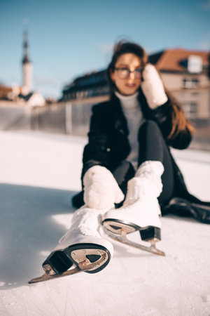 A young woman in winter attire sits on the ice, catching her breath after a skating session under a clear sky.の写真素材