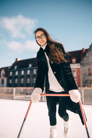 A young woman enjoys ice skating outdoors, smiling while balancing on a skating aid in winter.の写真素材