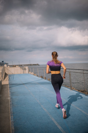 A woman runs along a coastal track under cloudy skies, enjoying the ocean breeze and scenic views.の写真素材