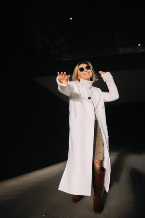 A woman wearing a white coat and sunglasses playfully poses indoors while enjoying her surroundings.の写真素材