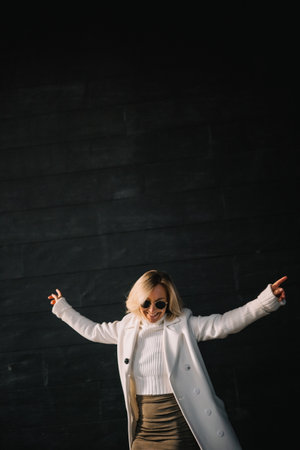 A woman in a white coat and sweater showcases her dance moves in a sunny urban area, exuding...