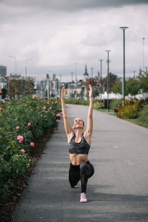 A woman performs lunges in a park vibrant with blooming flowers on a clear, sunny morning.の写真素材