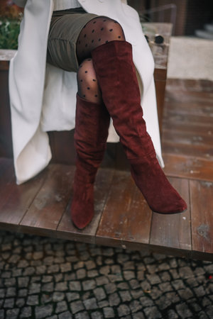 A woman in fashionable burgundy over-the-knee boots shows off her footwear while relaxing outdoors on a wooden platform.の写真素材