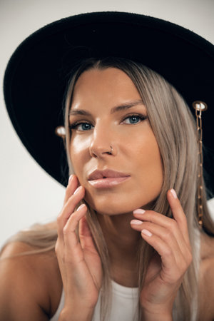 A model showcases natural beauty while posing with a black hat and elegant makeup in a neutral space.の写真素材