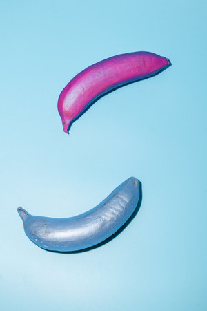 Two creatively painted bananas in vibrant pink and silver lay against a bright blue background, highlighting art.の写真素材