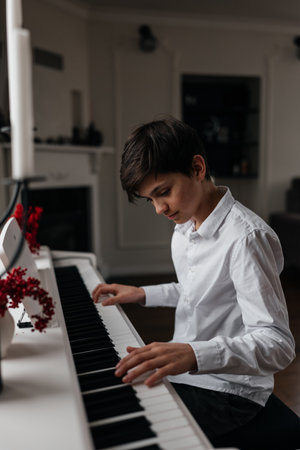 Handsome 12 years old boy in white shirt playing digital piano. Practicing at home. Focus on handsの写真素材