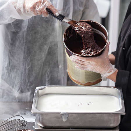 Women hands in gloves preparing chocolate ice cream - pouring chocolate ganache in stainless steel trayの写真素材