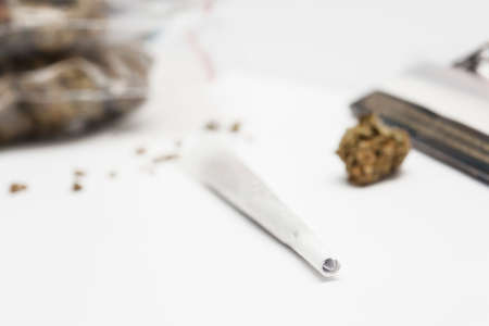 Preparing a cannabis joint with tobacco and rolling paper with marijuana bud on white background. The insinuation of marijuana abuse.の写真素材