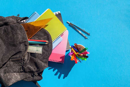Overview of schhol bag and its content on a blue background. Backpack with school supplies - notebooks, penciles, divider and rulerの写真素材