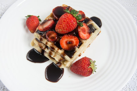 Delicious waffle with strawberries and chocolate syrup on a white dishの写真素材