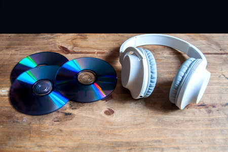 Compact disc and headset on top of a wooden table with black background