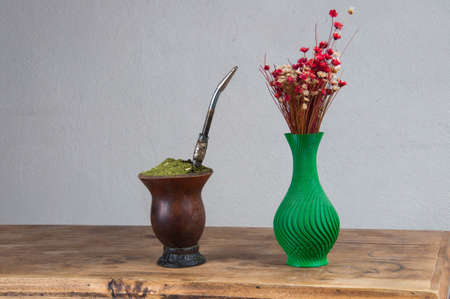 chimarrÃ£o cuia next to a flower vase on top of a wooden table