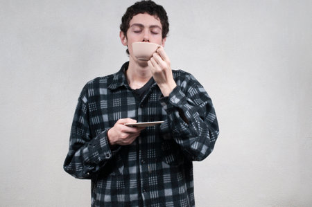 Man in plaid shirt sipping coffee with neutral backgroundの写真素材