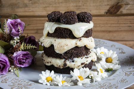 Chocolate cake with cream and chamomile flowers on wooden background