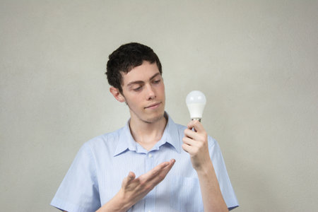 Young man holding a lightbulb in his hand and looking at itの写真素材