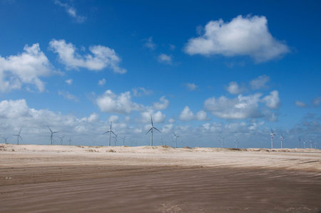 Wind turbines on a sandy beach with blue sky and white clouds.