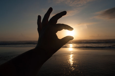 Silhouette of hand showing ok sign on the beach at sunsetの写真素材