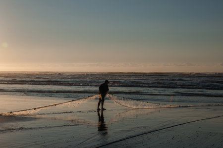Silhouette of fisherman casting net on the beach at sunrise.のeditorial素材