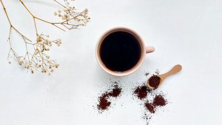 Cup of coffee with ground coffee and dried flowers on white background
