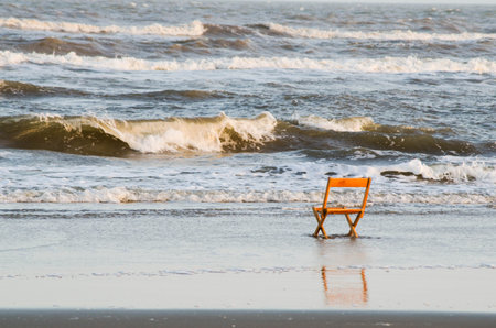 Wooden chair on the beach with sea waves in the background.の写真素材