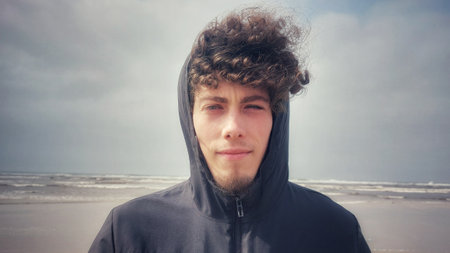 Young man with curly hair in a hoodie on the beachの写真素材
