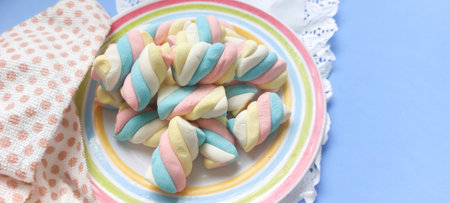 Colorful marshmallows on a plate on a blue background.