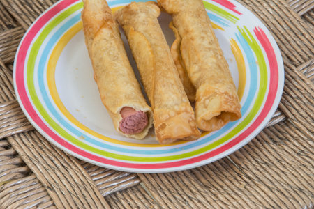 Fried spring rolls with sausage in a plate on wicker background