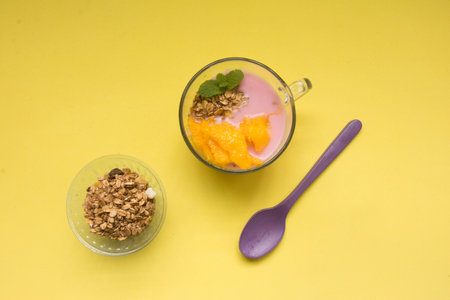Yogurt with mango and granola in glass on yellow backgroundの写真素材