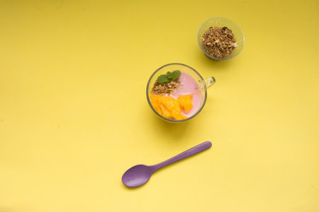 Mango, yogurt with granola and mint leaves on yellow background.