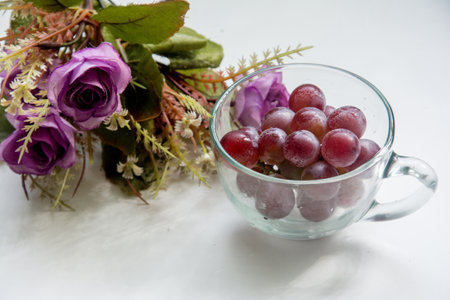 grapes in a glass cup on a white background with purple flowersの写真素材