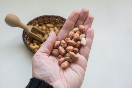 Close up of peanuts in hand with wooden scoop on white background.
